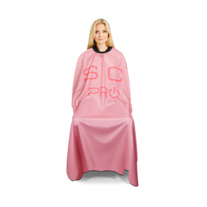 A blonde model wearing a pink salon cape with 'SC PRO' printed in pink on the front, set against a plain white background.