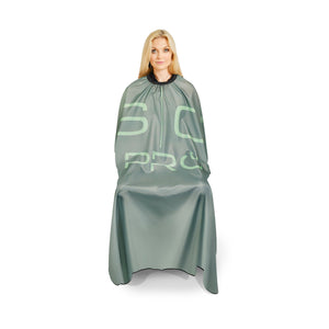 A woman wearing a sage green hairdressing cape with light green 'SC PRO' lettering, shown against a plain white background.