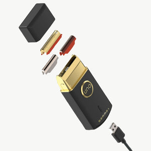 A black and gold Gamma+ Uno shaver charging case with a USB-C cable, shown with several small disassembled components floating around it on a textured gray background.