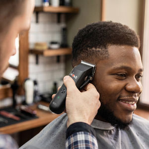 A close-up lifestyle shot of a barber using a homie nano hair clipper to trim a client's hair in a salon setting.