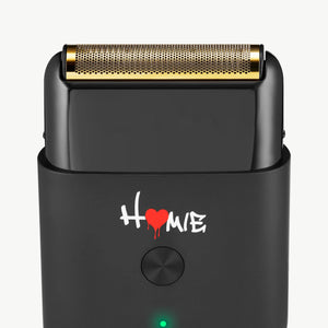 A close-up of Homie Nano Single Foil Shaver with a gold-toned metal shaving head and a white 'HOME' logo with a red heart on the front, set against a plain white background.