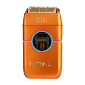 An orange electric shaver with a metallic finish, featuring a circular blue accent line, the brand name 'INSTINCT' printed in silver on the front, and 's|c' near the shaving head. The shaver is shown against a plain white background.