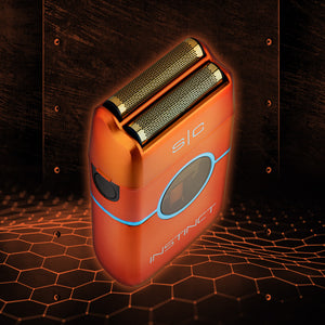 An orange electric shaver with gold metallic blades and blue accent lines, shown at an angle against a dark wood panel background with a glowing orange hexagonal pattern on the floor.