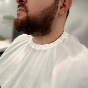 A close-up of a man's lower face and neck wearing a white barber-style neck drape or salon cape.