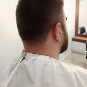 Back view of a person with a haircut in a salon setting showing clasp of cutting cape
