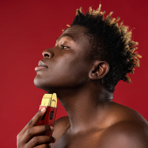 Man with styled hair holding a red and gold grooming tool against a red background