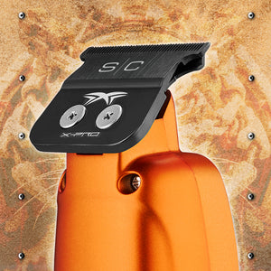 Close-up of an orange cordless clipper with a black guard clip labeled S/C and X-Pro, shown against a textured metallic background.