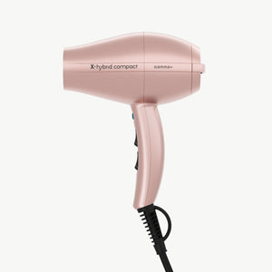 A compact X-hybrid compact hair dryer in a metallic rose gold finish, shown from a side profile view against a solid white background. The brand name 'gamma+' is printed on the side of the dryer.