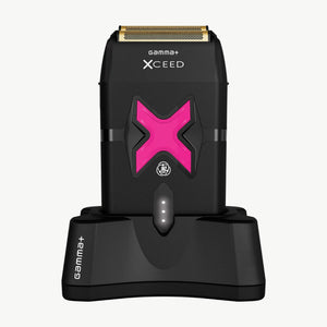 Xceed Gamma+ electric shaver with a metallic gold blade and a prominent pink 'X' accent, shown standing on its matching black charging dock against a white background.
