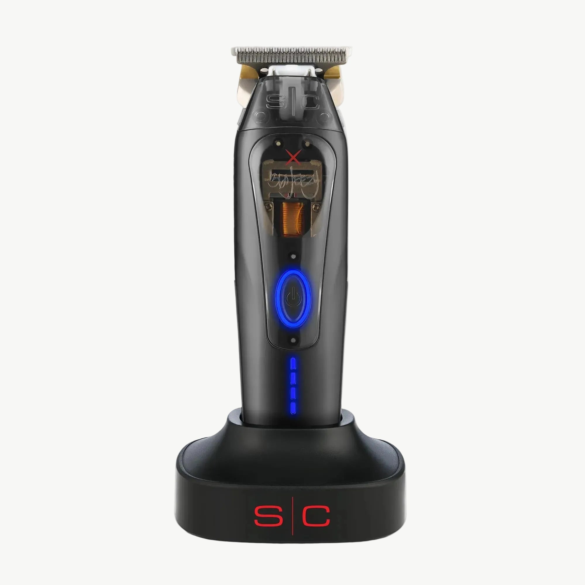 360 X Jeezy trimmer standing upright on a matching black charging dock against a plain white background. The shaver has a blue circular control button, a small display screen, and metallic silver blades at the top.
